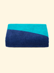 Modèle "Swell" de serviette de plage Tucca 100% coton biologique, parfaitement pliée comme présentée sur l'emballage, avec deux épingles de chaque côté, celles qui peuvent être utilisées pour fixer votre serviette de plage au sable.