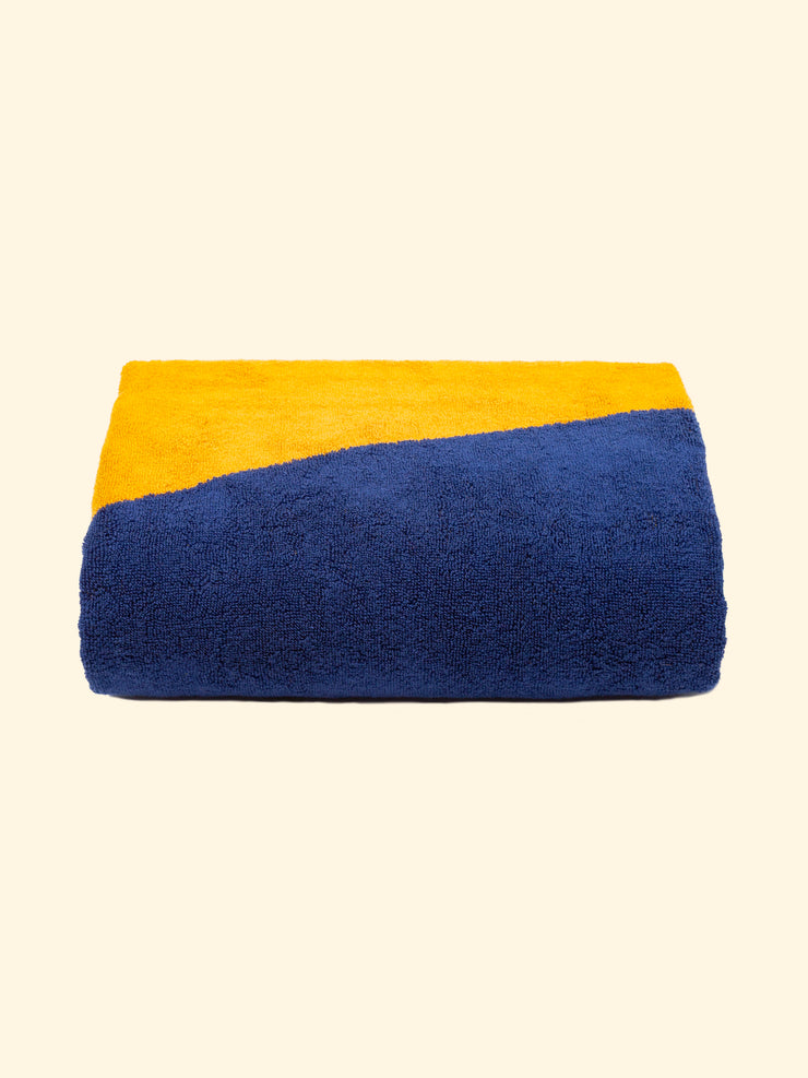 Modèle "Dune" de serviette de plage Tucca 100% coton biologique, parfaitement pliée comme présentée sur l'emballage, avec deux épingles de chaque côté, celles qui permettent de fixer votre serviette de plage au sable.