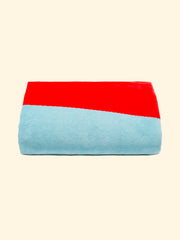Serviette de plage modèle Berry of Tucca parfaitement pliée comme présenté sur l'emballage, avec deux épingles de chaque côté, celles qui peuvent être utilisées pour fixer votre serviette de plage au sable.