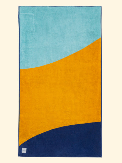 Tucca "Dune" beach towel extended. Light blue, camel yellow and dark blue colors in big blocks composing a beautiful design. Large beach towel that doesn't get blown by the wind. Thick and soft texture as it is made with 100% organic cotton.