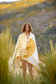 Fille se couvrant avec la Tucca style "Danai". Une serviette de plage extra légère qui ne se laisse pas emporter par le vent. Texture super douce car elle est fabriquée en coton 100% biologique.